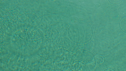 Kräuselungen von Wassertropfen, Kreise auf Türkis blauem Wasser, Pool, See, glatte Wasseroberfläche, abstrakter Hintergrund verwischt.mit Raum für Text.