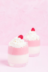 Raspberry panna cotta decorated with cream and ripe berry on pastel pink background.