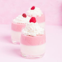 Raspberry panna cotta decorated with cream and ripe berry on pastel pink background.