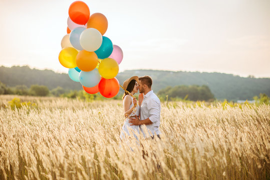 Love couple with balloons hugs in a rye field
