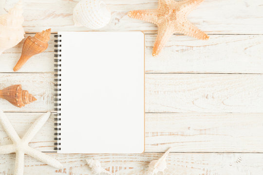 Blank notebook and seashells on white wooden floor.