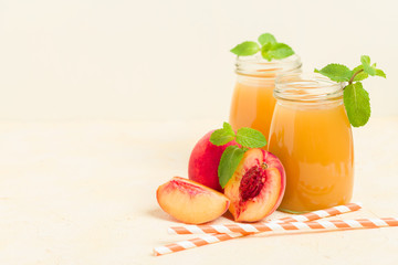 Peach smoothie in glass jars with fresh ripe fruits and green mint leaves on yellow pastel background.