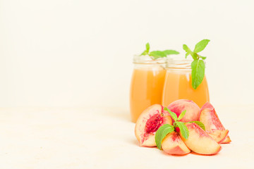 Peach smoothie in glass jars with fresh ripe fruits and green mint leaves on yellow pastel background.