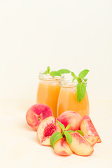 Peach smoothie in glass jars with fresh ripe fruits and green mint leaves on yellow pastel background.