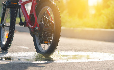 the child is riding a bicycle close-up passing through a puddle and splashing water in the rays of...