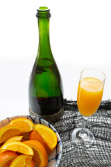 Glass of mimosa cocktail ready to be served for brunch with an orange slice with a champagne bottle and a bowl of orange slices on a white table