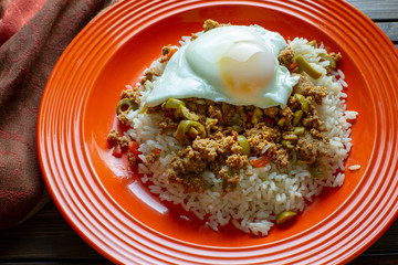 Picadillo a Cuban dish made of ground beef served on a bed of rice with a sunny side up egg on a red plate on a wooden kitchen table