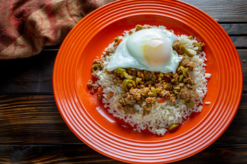Picadillo a Cuban dish made of ground beef served on a bed of rice with a sunny side up egg on a red plate on a wooden kitchen table