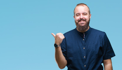 Young caucasian hipster man over isolated background smiling with happy face looking and pointing to the side with thumb up.