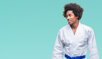 Afro american man wearing karate kimono over isolated background looking away to side with smile on face, natural expression. Laughing confident.