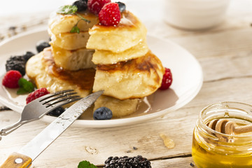 Pancakes with forest fruits berries on white table.