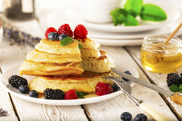 Pancakes with forest fruits berries on white table.