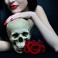 Brunette witch holding human skull and red roses. Halloween art design gothic portrait.