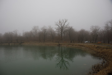 Amazing landscape of bridge reflect on surface water of lake, fog evaporate from pond make romantic scene or Beautiful bridge on lake with trees at fog.