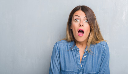 Young adult woman over grunge grey wall wearing denim outfit afraid and shocked with surprise expression, fear and excited face.