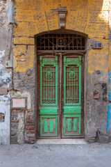 Old grunge green decorated painted door on dirty yellow painted stone wall, Old Cairo, Egypt