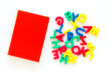 Children learn read concept. Plastic letters of toy alphabet near book on white background top view