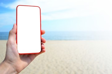 The hand holds the smarts in the hand against the background of the sea. Place for text on the smartphone screen. Internet access on vacation, work on vacation