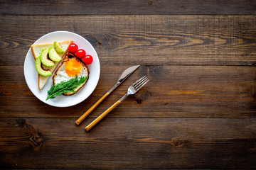 Healthy hearty breakfast. Fried eggs with vegetables near toast with avocado on dark wooden background copy space