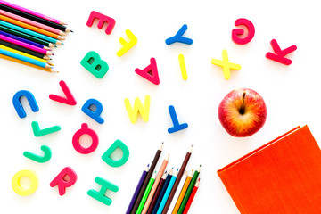 Primary school concept. Letters of english alphabet, book, apple and color pencils on white background top view