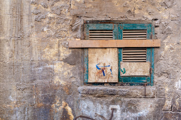 Old grunge window with closed green broken shutters on dirty cracked bricks stone wall