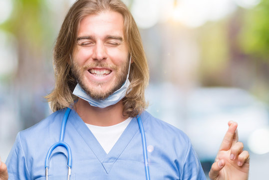 Young handsome doctor man with long hair over isolated background smiling crossing fingers with hope and eyes closed. Luck and superstitious concept.