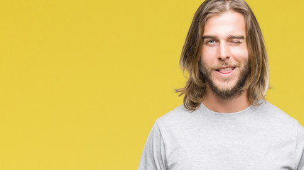 Young handsome man with long hair over isolated background winking looking at the camera with sexy...
