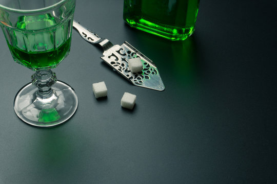 a glass of absinthe, a stainless steel slotted spoon with the sugar cubes and the absinthe bottle on the table