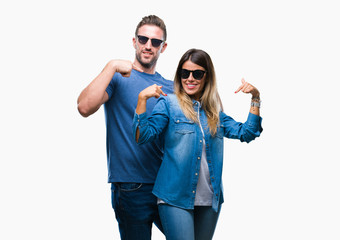 Young couple in love wearing sunglasses over isolated background looking confident with smile on face, pointing oneself with fingers proud and happy.