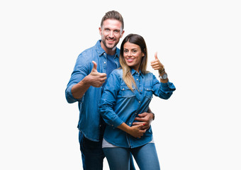 Young couple in love over isolated background doing happy thumbs up gesture with hand. Approving expression looking at the camera with showing success.