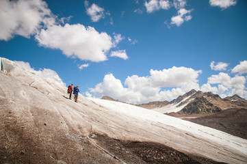 Two tourists, a man and a woman with backpacks and cats on their feet, stand on the ice in the background of the mountains of the sky and clouds. communication in the mountains