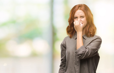 Young beautiful woman over isolated background smelling something stinky and disgusting,...
