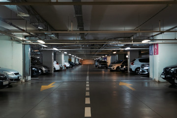 Illuminated underground car parking interior under modern mall with lots of vehicles and arrows on...