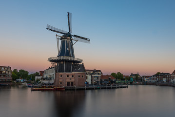 Fototapeta na wymiar Dutch windmill, in the town of Haarlem, at sunset. The water is smooth, due to a long shutter speed - room for copy