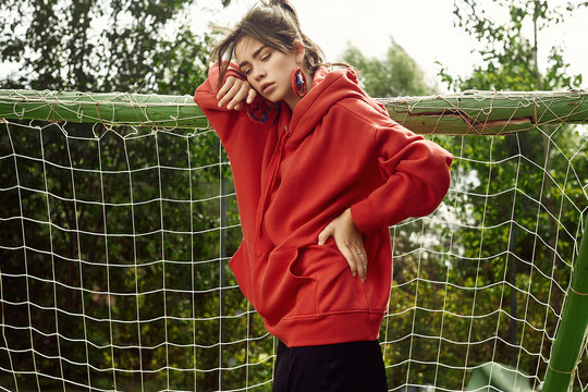 Gorgeous brunette woman in fashion red hoodie on sports field