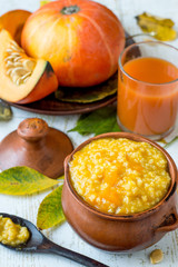 A small clay pot with millet porridge, a glass with natural freshly prepared juice and a fresh ripe pumpkin on an old wooden table.  The concept of healthy eating. 