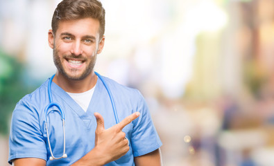 Young handsome doctor surgeon man over isolated background cheerful with a smile of face pointing with hand and finger up to the side with happy and natural expression on face looking at the camera.