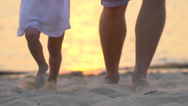Little baby learns to walk. First Steps. Slow Motion 120 fps. Father is teaching him child, litle girl to do the first steps on a sand on the beach in summer. Close up on feet. Happy childhood. Happy