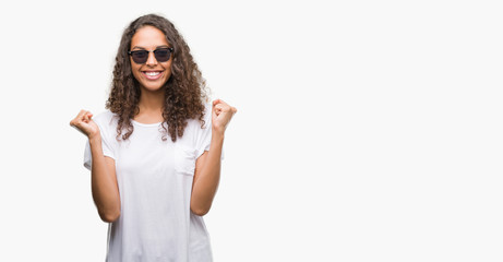 Young hispanic woman wearing sunglasses celebrating surprised and amazed for success with arms raised and open eyes. Winner concept.