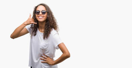 Young hispanic woman wearing sunglasses smiling doing phone gesture with hand and fingers like talking on the telephone. Communicating concepts.