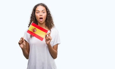 Young hispanic woman holding flag of Spain scared in shock with a surprise face, afraid and excited with fear expression