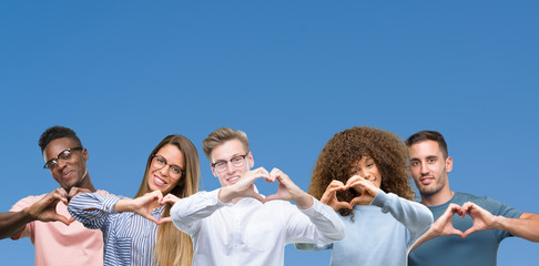 Composition of group of friends over blue blackground smiling in love showing heart symbol and shape with hands. Romantic concept.