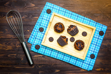 Top view of fresh homemade delicious vanila and chocolate muffins in paper cupcake holder with cookie and cream isolated on napkin, tablecloth on wooden background.