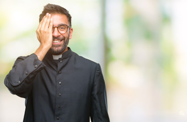 Adult hispanic catholic priest man over isolated background covering one eye with hand with confident smile on face and surprise emotion.