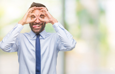 Adult hispanic business man over isolated background doing ok gesture like binoculars sticking tongue out, eyes looking through fingers. Crazy expression.