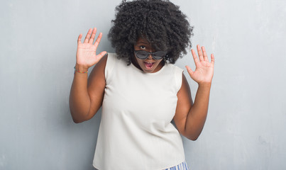 Young african american plus size woman over grey grunge wall wearing fashion sunglasses afraid and...