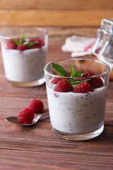 chia pudding in a glass with raspberries on a wood background.