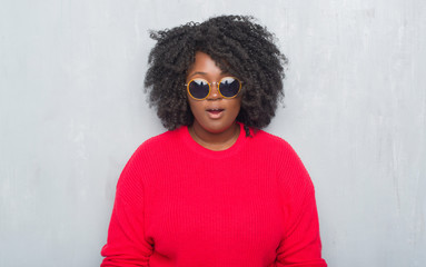 Young african american plus size woman over grey grunge wall wearing retro sunglasses afraid and shocked with surprise expression, fear and excited face.