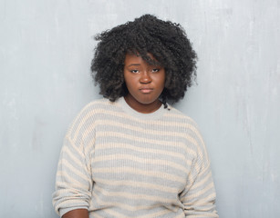 Young african american plus size woman over grey grunge wall wearing a sweater depressed and worry for distress, crying angry and afraid. Sad expression.