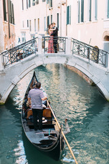Fototapeta na wymiar Venetian scenery with a gondola on a narrow canal. Romantic couple standing on the bridge of venetian canal.